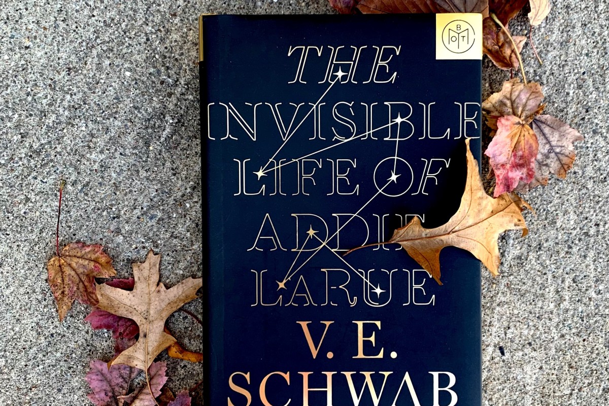 A Book of the Month copy of The Invisible Life of Addie LaRue by V.E. Schwab. The book sits on concrete and is surrounded by fall leaves.